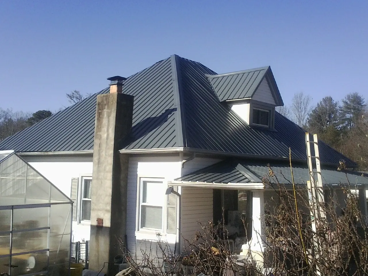 Dark blue standing seam metal roof on a white farmhouse with dormer — Slate & Tile Roof Repair by Roofing Brothers in Fowlerville