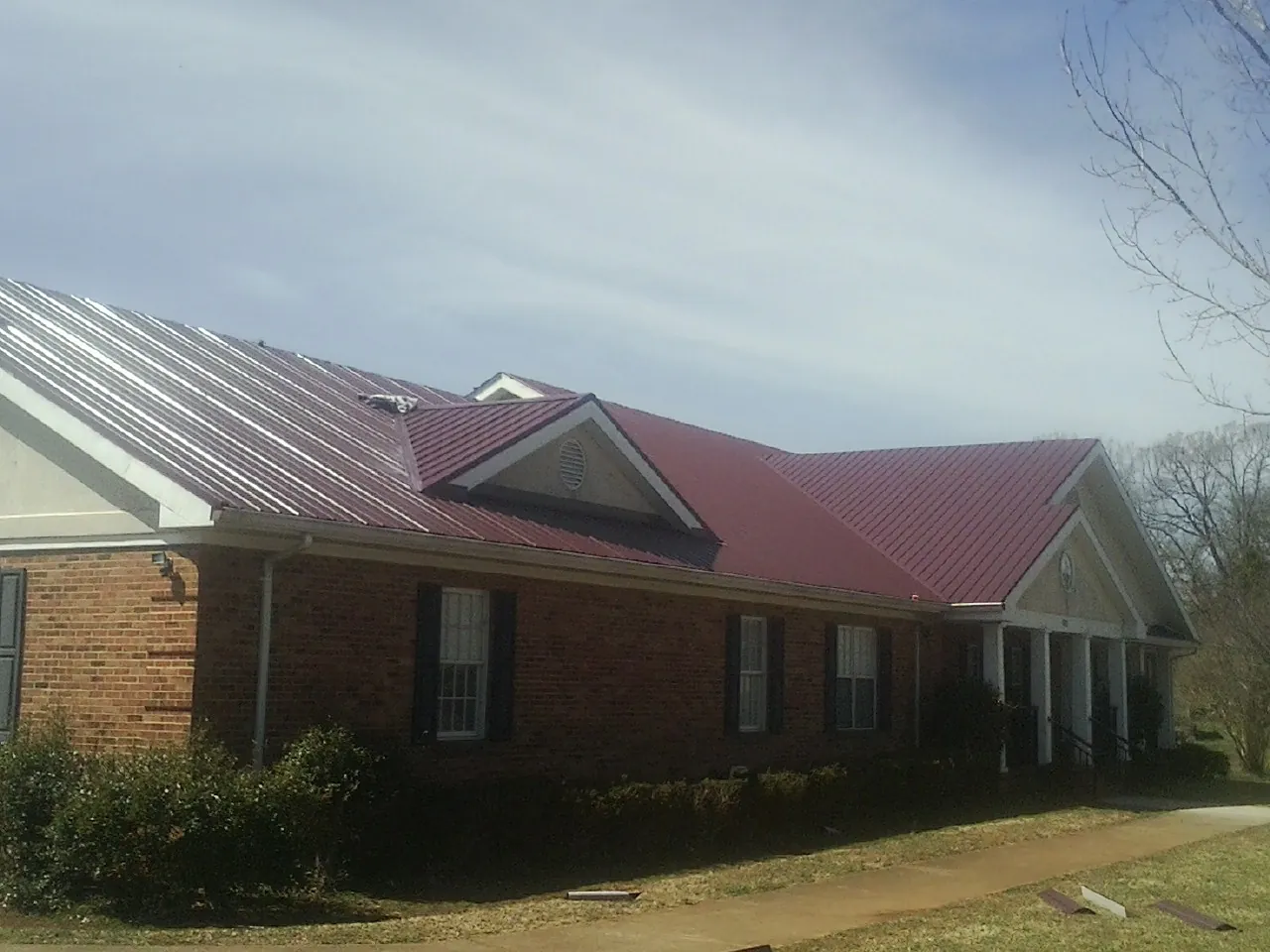 Red metal roof with gabled entries on a long brick building, from a Hail Damage Roof Repair job in Fowlerville