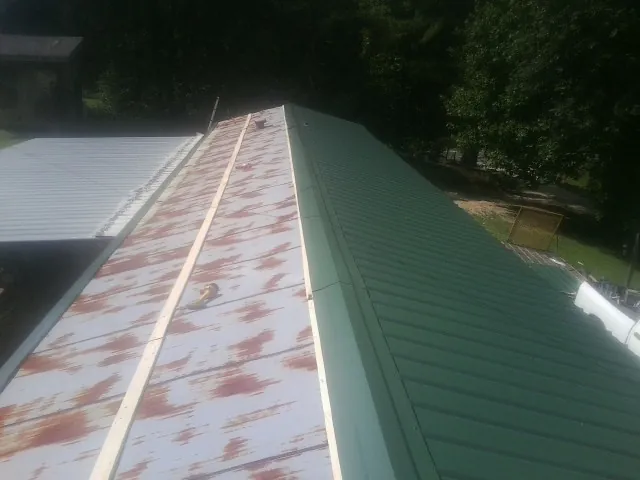 Old rusted panels beside newly installed green metal roofing — Wind Damage Roof Repair by Roofing Brothers in Fowlerville