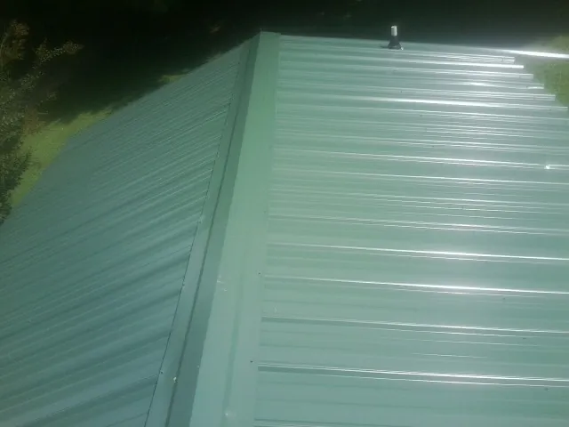 New green metal panels meeting at the ridge of a roof — Flat Roof Repair work by our crew in Fowlerville