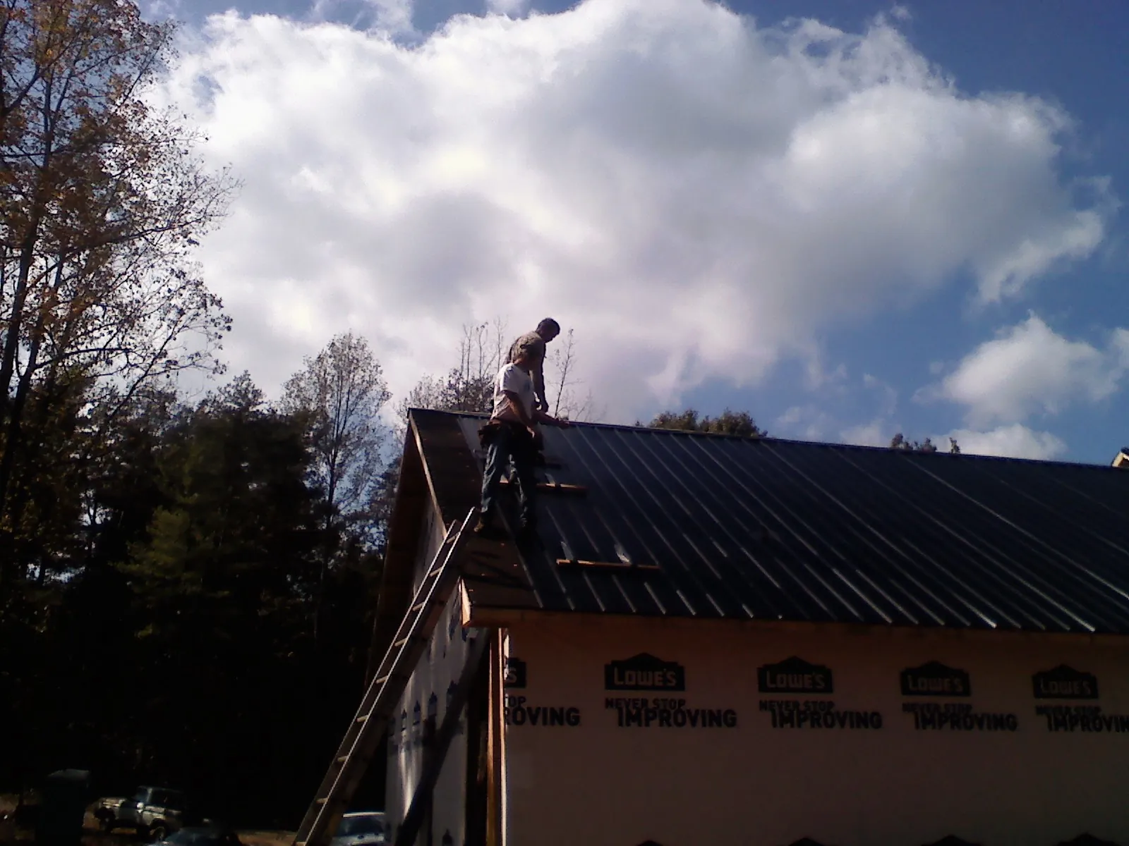 Roofer fastening dark metal panels high against a cloudy sky, from a Roof Inspection job in Fowlerville