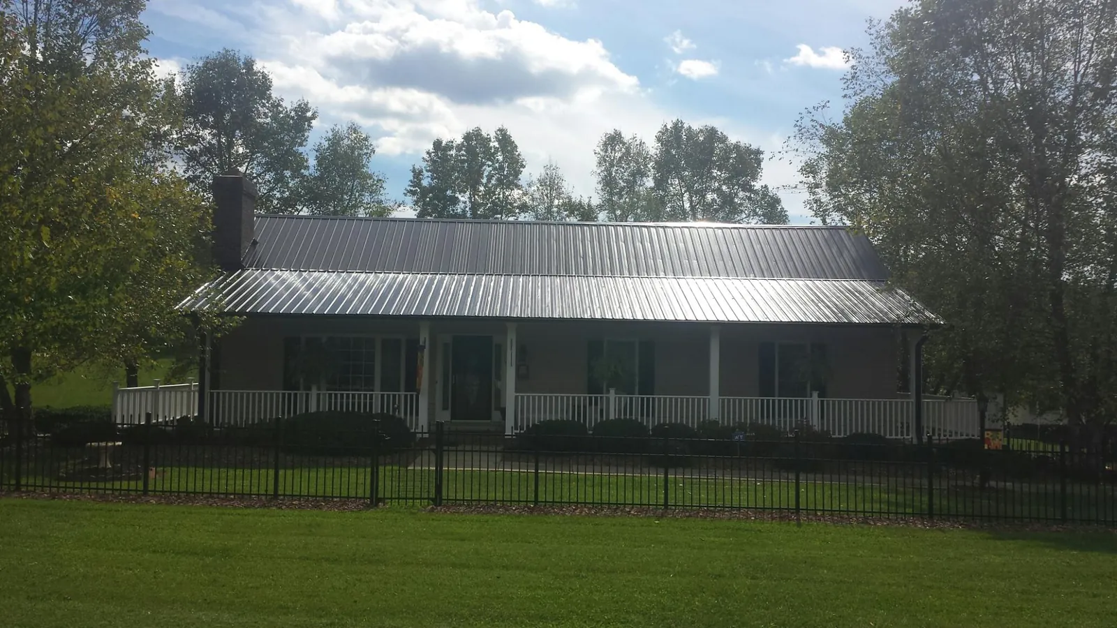 Gray metal roof on a brick ranch with a full width front porch — Gutter Guard Installation work by our crew in Fowlerville