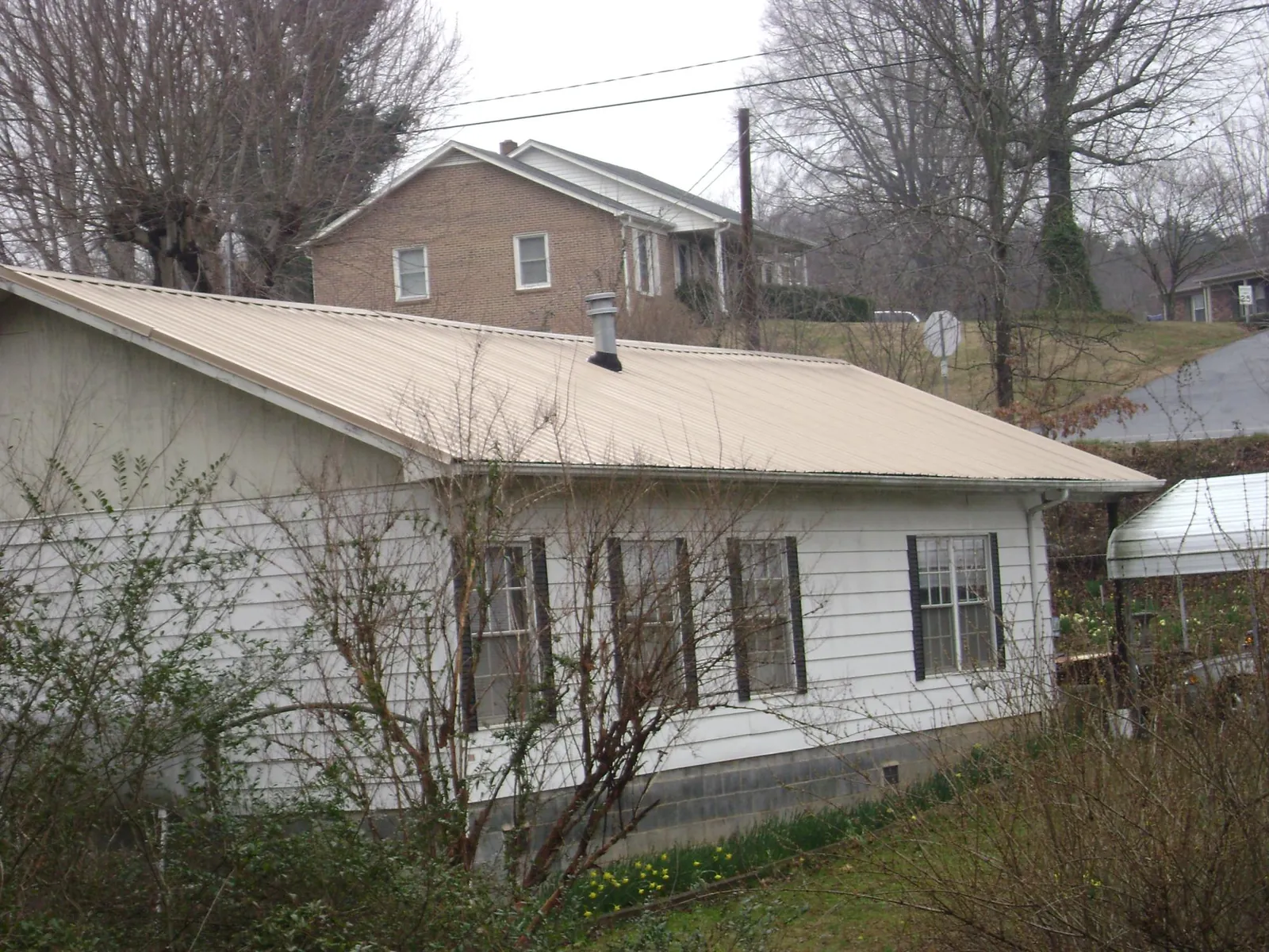Tan metal roof on a white sided house set into a hillside — Commercial Roofing by Roofing Brothers in Fowlerville