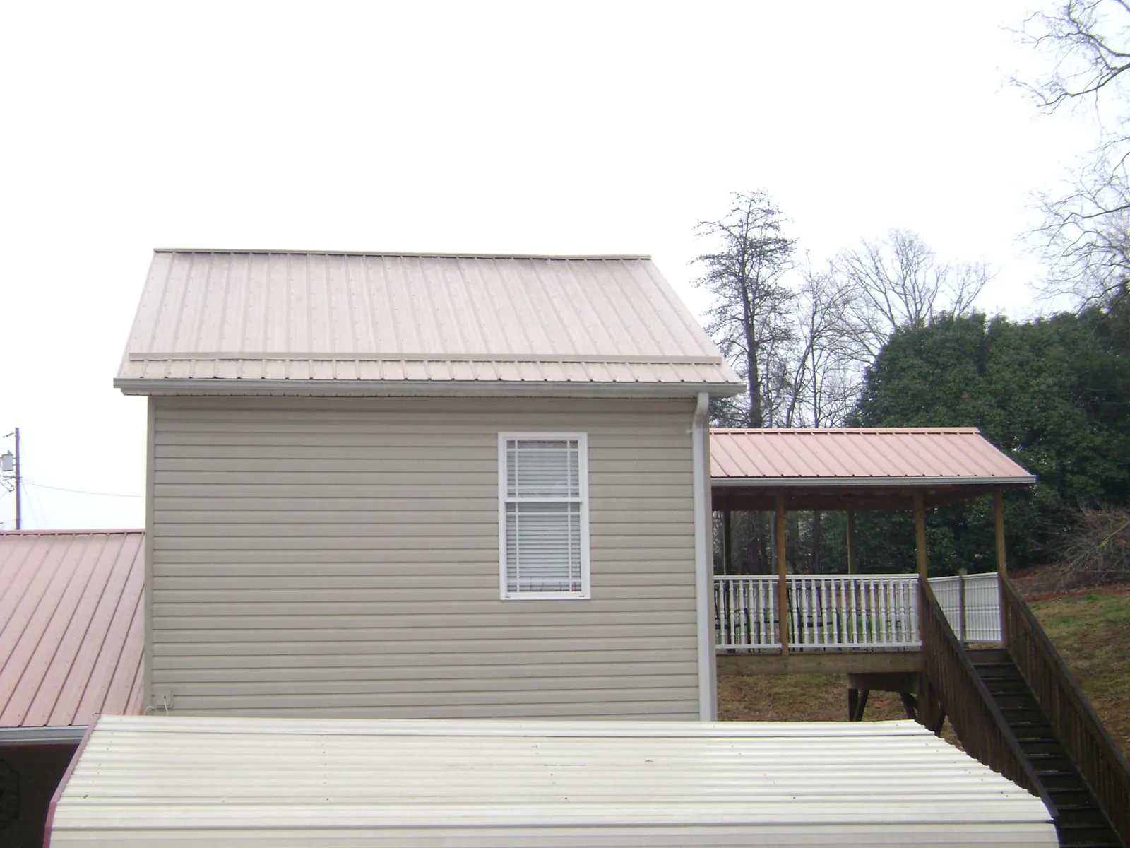 Tan metal roofs on a two story addition and attached porch, from a Roof Replacement job in Fowlerville