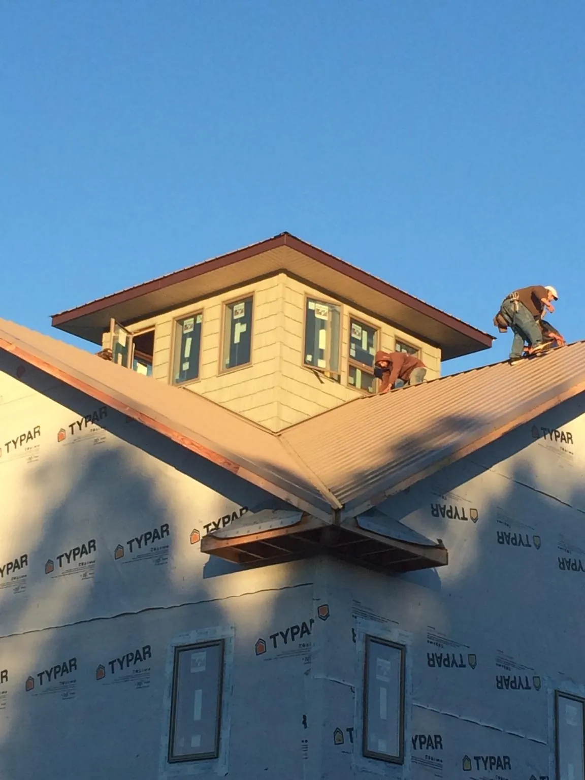 Roofers working around a rooftop cupola on a new metal roof at sunset — Roof Waterproofing in Fowlerville by Roofing Brothers